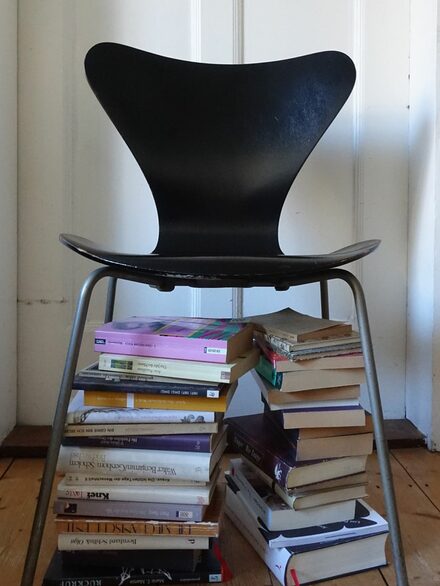 Bücher sind unter einem Stuhl gestapelt.